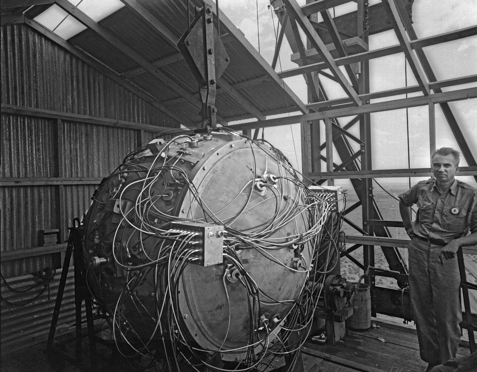 Norris Bradbury, group leader for bomb assembly, stands next to the partially assembled Gadget atop the test tower during the Trinity test. 